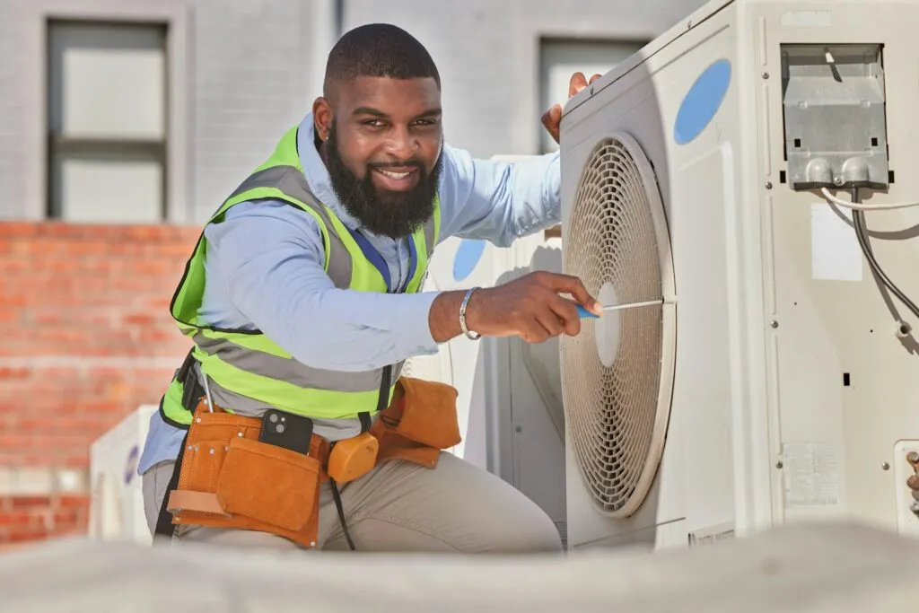 Black technician in safety gear performing maintenance on an outdoor air conditioning unit, showcasing HVAC repair expertise relevant to Maverick Ambitions HVAC services in Newark, NJ.